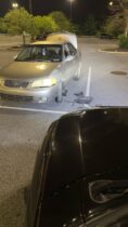 Gold Nissan Sentra with spare tire on front driver's corner, jack and tools laid out, photographed from the windshield of a black Toyota FJ Cruiser. This is how to change a tire.