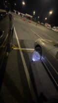 How to change a tire with a portable air compressor hose connected to compact spare tire on a sedan in a parking lot at night.