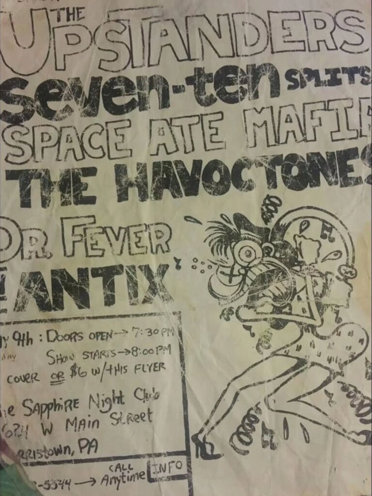 Crumpled black-and-white punk show flyer on yellowed paper advertising a mid-90s gig at the Sapphire Night Club in Norristown, Pennsylvania. The top half is packed with hand-drawn band names in rough block letters — The Upstanders, Seven-Ten Splits, Space Ate Mafia, The Havoctones, Dr. Fever, and Antix — above handwritten details about doors at 7:30 p.m., an 8:00 p.m. start, and a cheaper cover “with this flyer.” The right side features a chaotic cartoon figure with wild hair and exaggerated limbs, drawn in the same photocopied, DIY style.