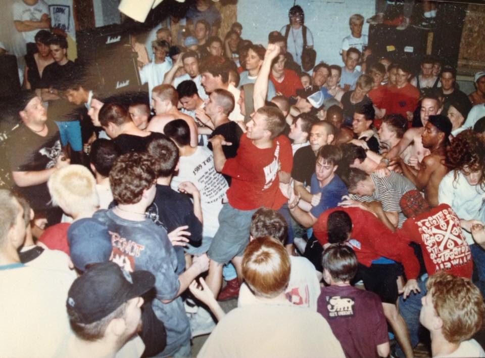 Crowded mosh pit at a small punk show inside Unisound in Reading, Pennsylvania, with fans packed shoulder to shoulder, arms raised and bodies colliding in front of the band on a cramped stage.