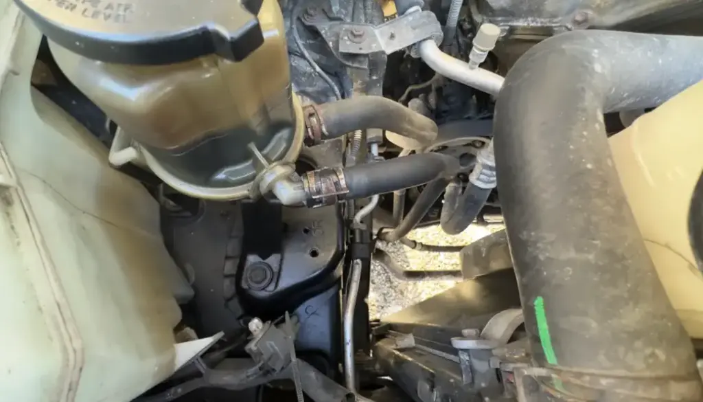 Power steering reservoir on a 2007 Toyota FJ Cruiser showing the return and feed hoses and hose clamps. This is where a Power Steering Fluid Flush begins