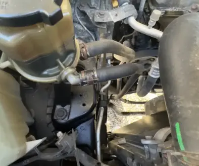 Power steering reservoir on a 2007 Toyota FJ Cruiser showing the return and feed hoses and hose clamps. This is where a Power Steering Fluid Flush begins