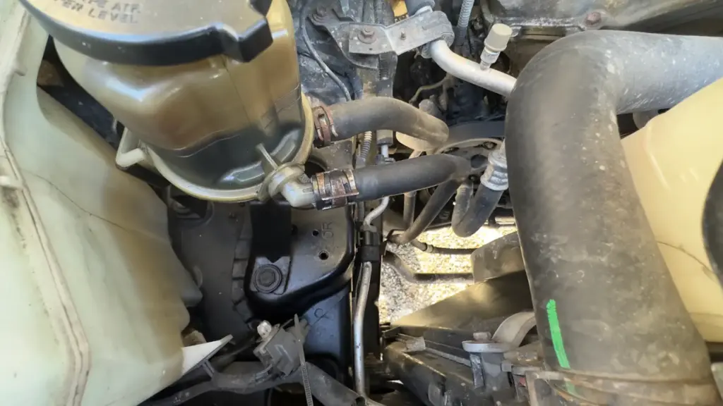 Power steering reservoir on a 2007 Toyota FJ Cruiser showing the return and feed hoses and hose clamps. This is where a Power Steering Fluid Flush begins