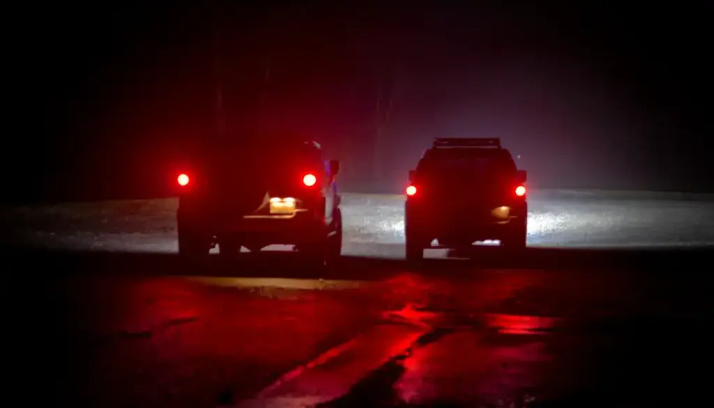 Two 2007 Toyota FJ Cruisers stopped on a wet road at night in light fog, red taillights glowing and reflecting on the pavement. Featured image for the Back on Track field note.
