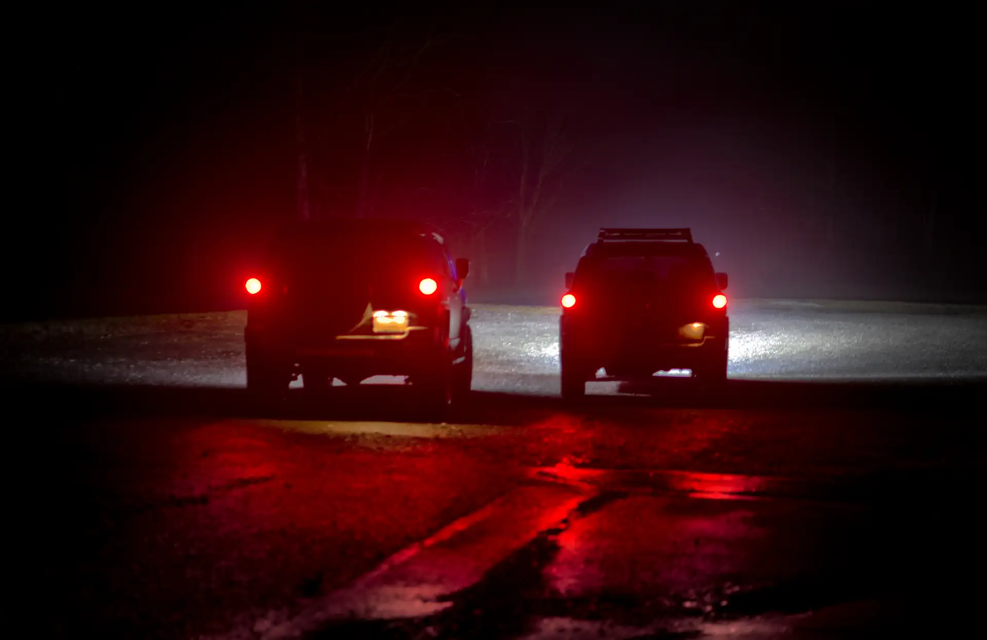 Two 2007 Toyota FJ Cruisers stopped on a wet road at night in light fog, red taillights glowing and reflecting on the pavement. Featured image for the Back on Track field note.