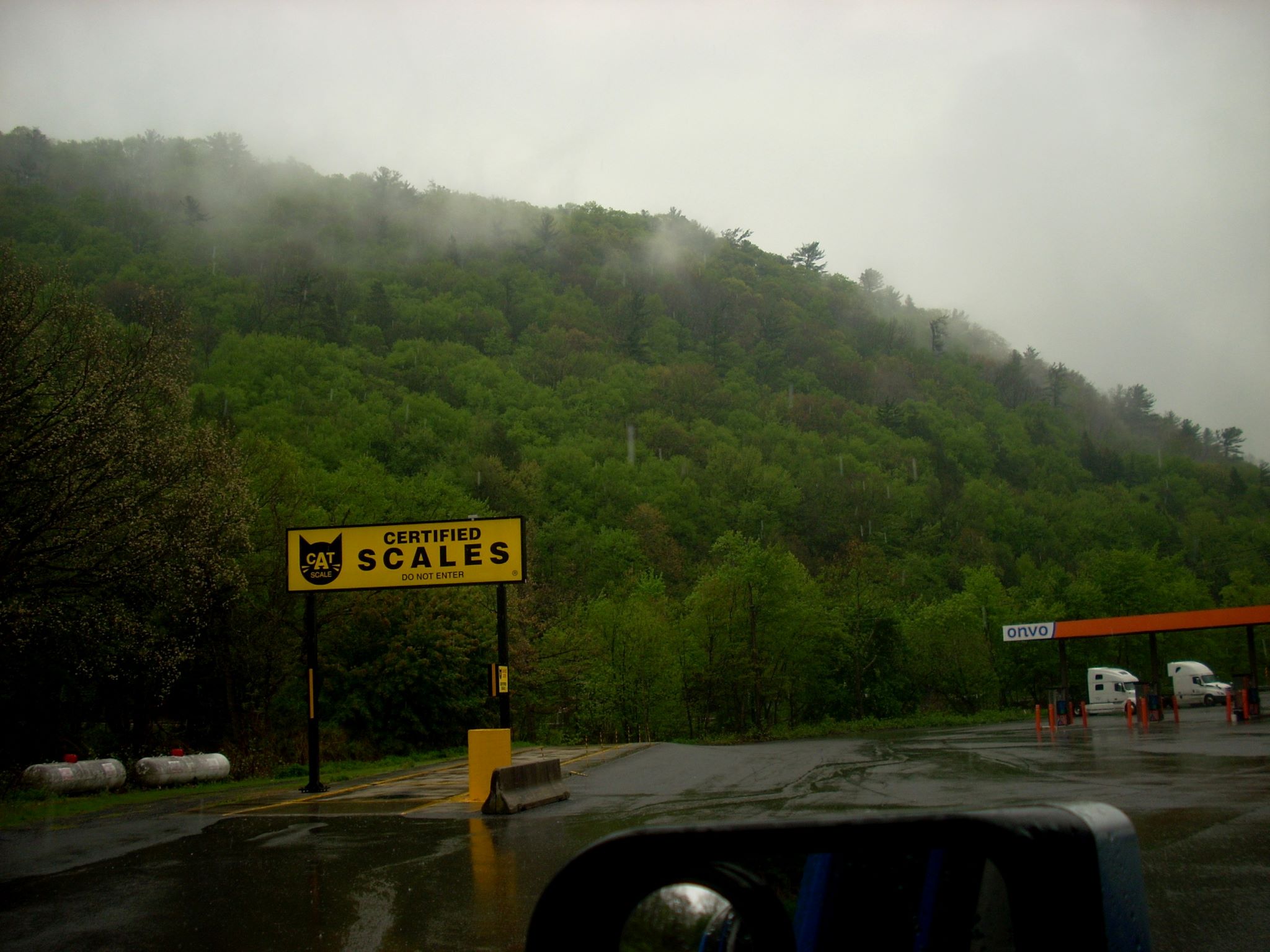 DSCN0398r Image of a tree covered hill dappled in mist rising above the rain-shined parking lot of a truck stop with a CAT certified scale in the foreground.